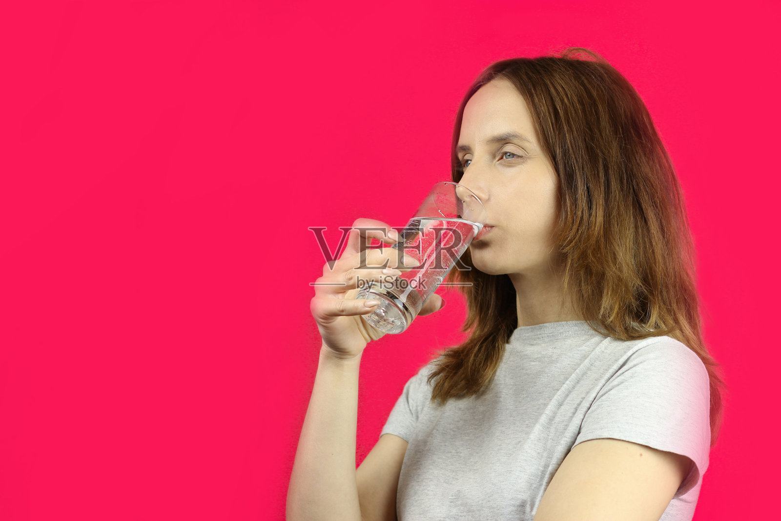 长头发的女孩在粉红色的背景上喝水，复制空间照片摄影图片