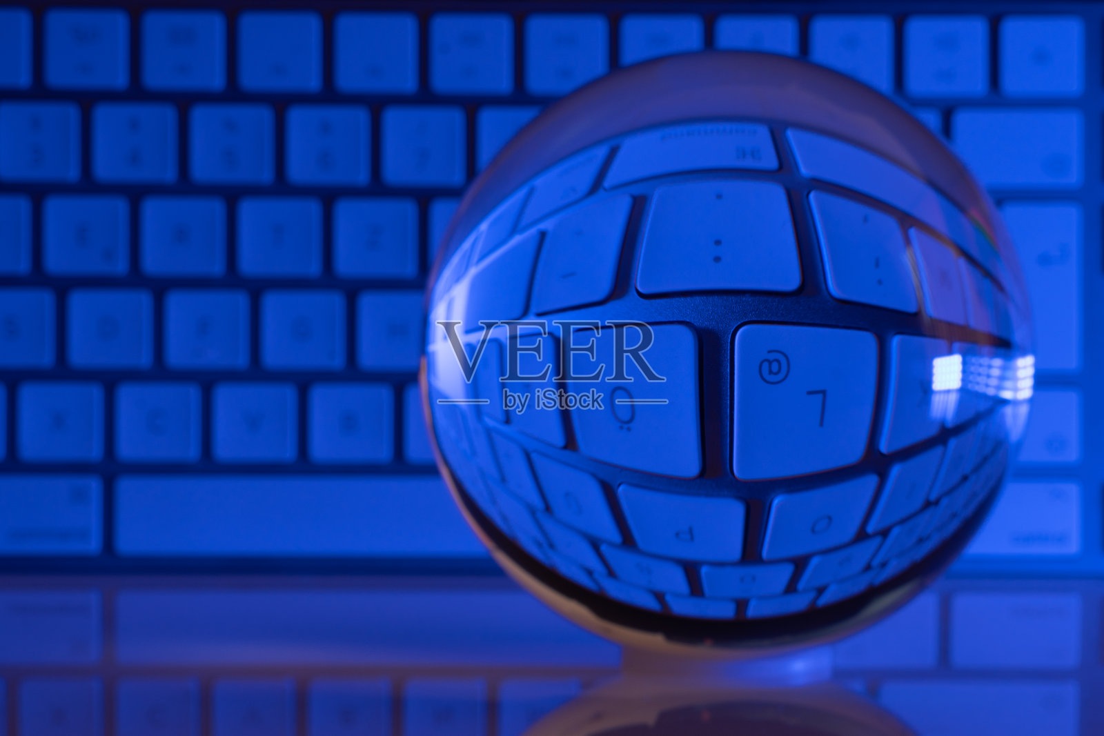 一个水晶般透明的玻璃球放在一个白色的电脑键盘前，我们被照亮了照片摄影图片