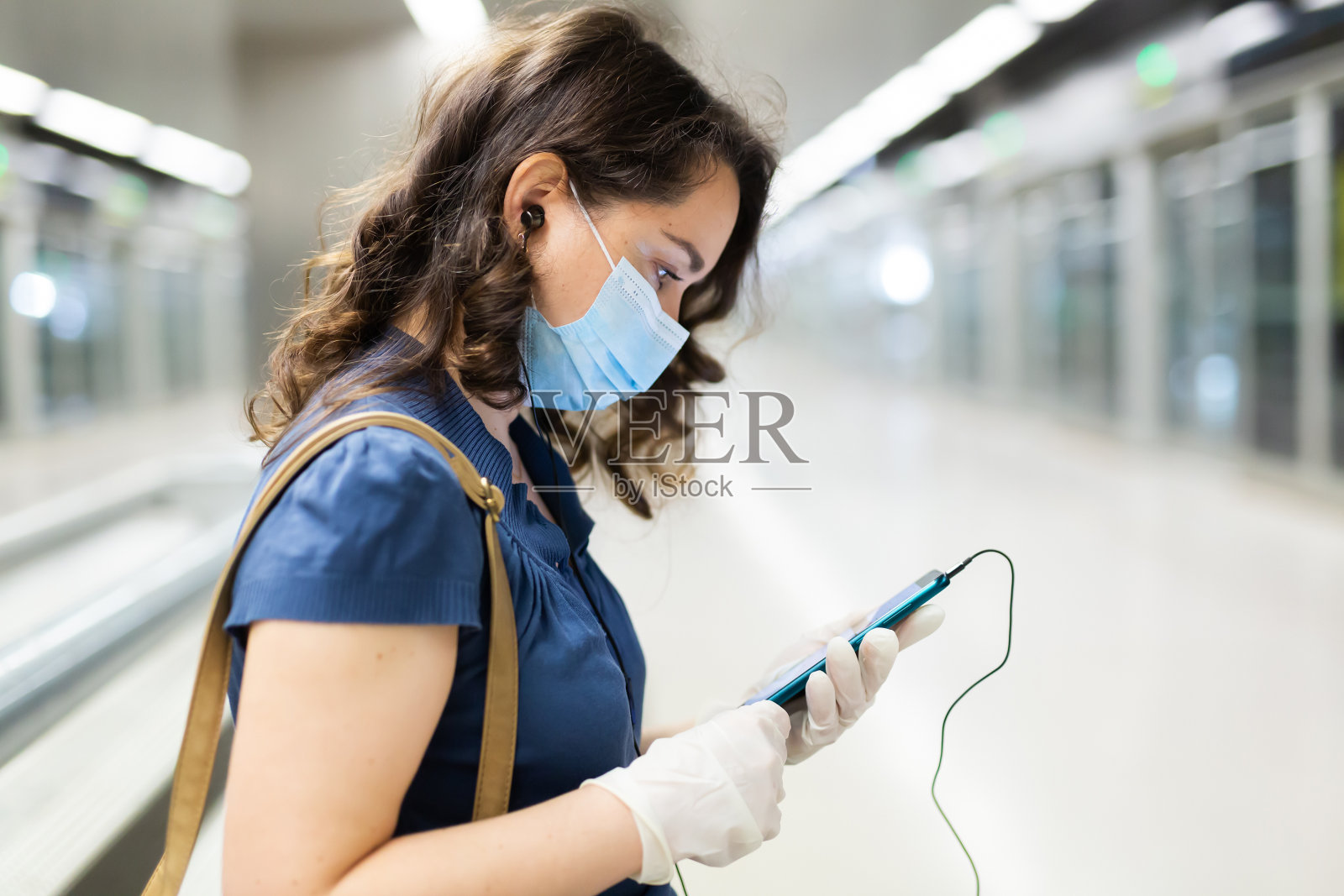 戴着医用口罩的黑发女子在地铁站台上打电话照片摄影图片