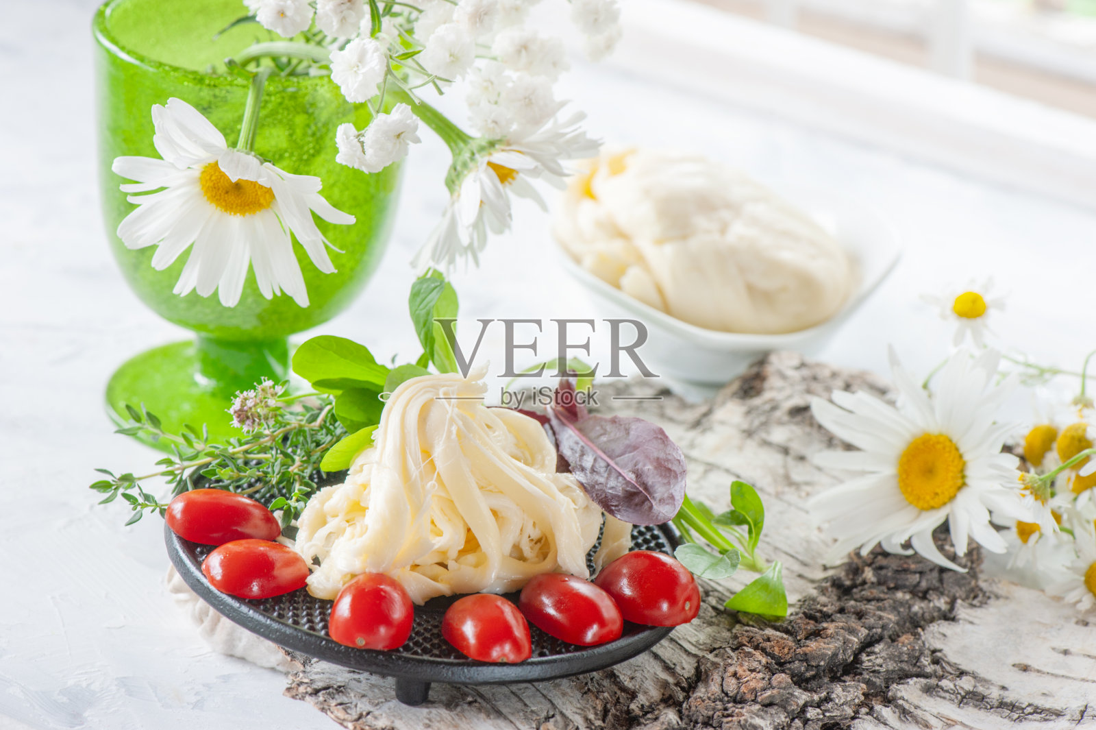 传统的白色纤维塞西尔奶酪躺在盘子里。奶酪用成熟的西红柿和醋栗作装饰照片摄影图片