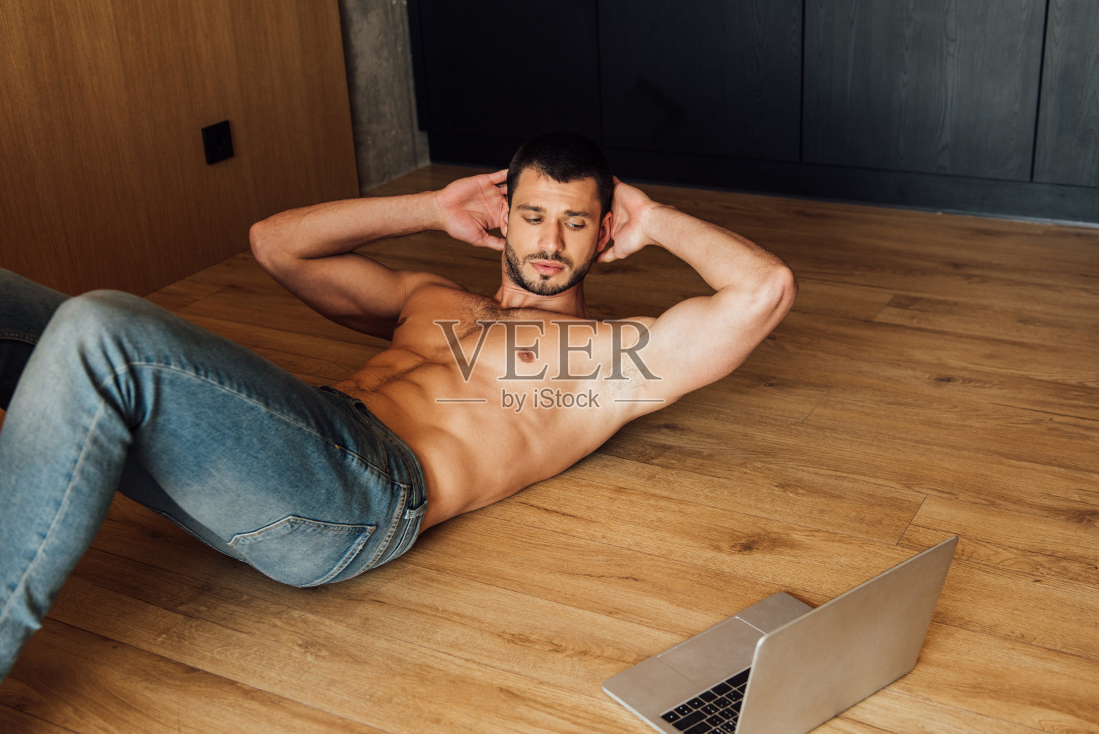 肌肉男一边锻炼一边在笔记本电脑上看在线训练照片摄影图片