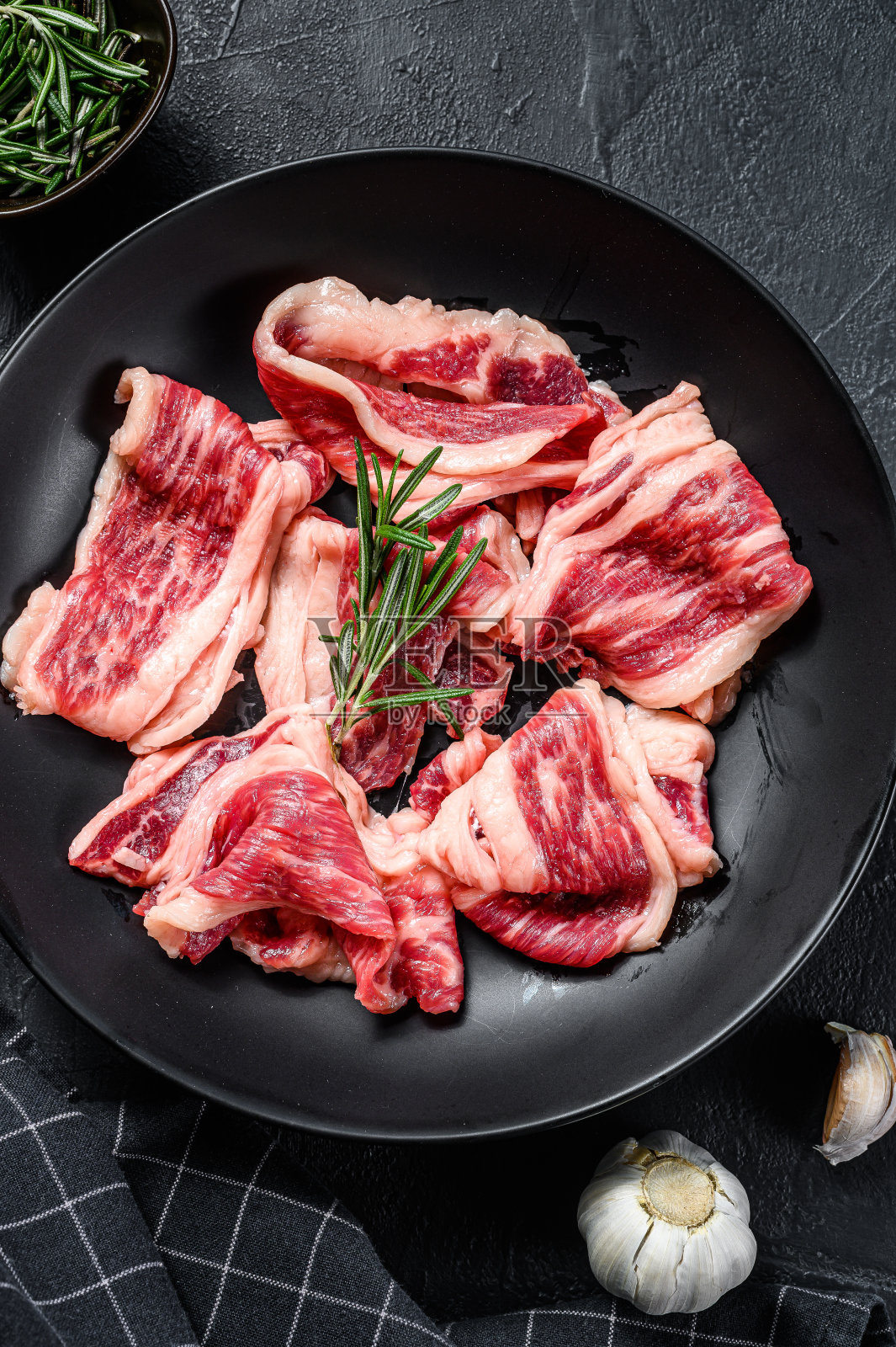 生牛肉培根，有大理石花纹的肉放在盘子里。黑色背景。俯视图照片摄影图片