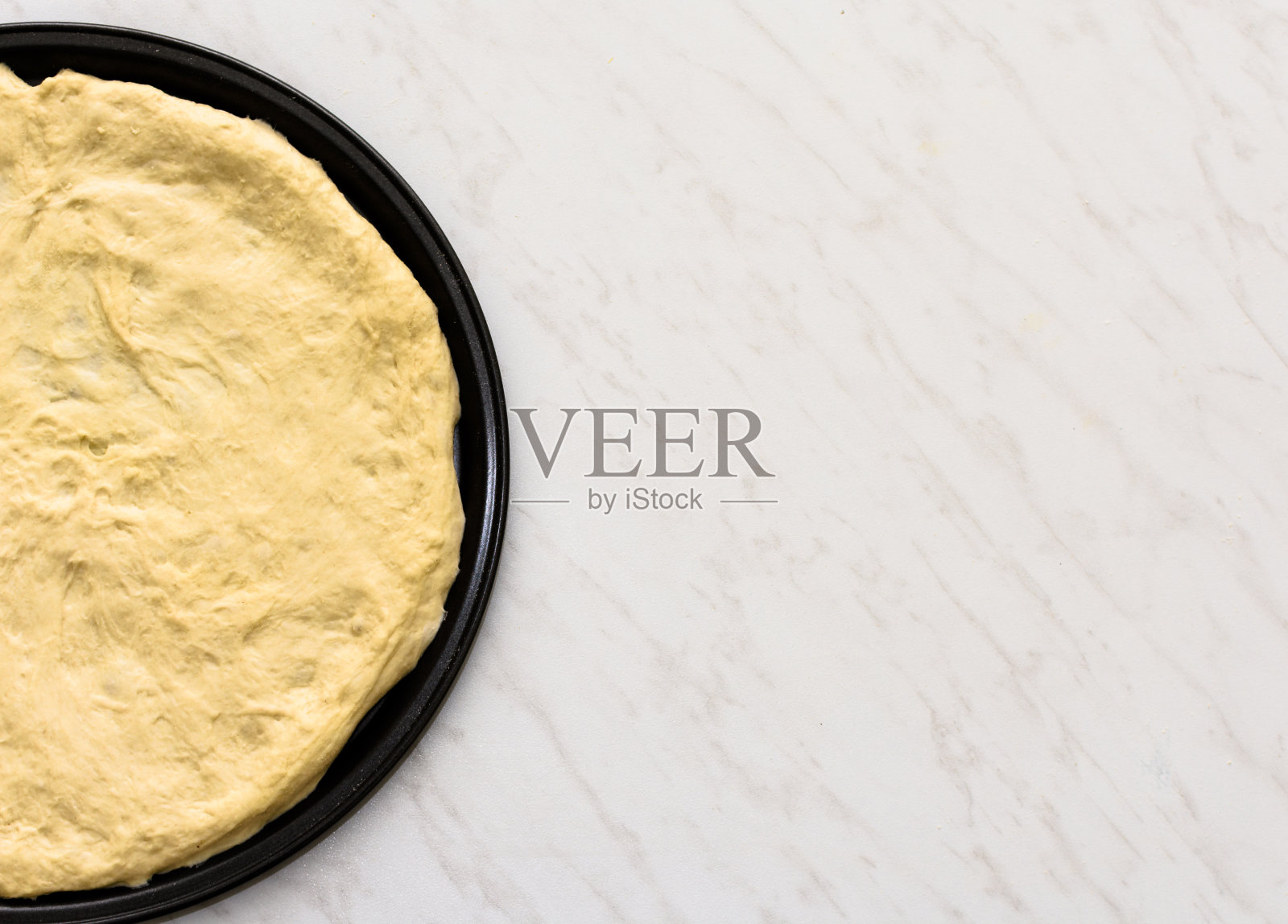 制作披萨，将披萨面团平铺在圆形烤盘上，放在白色的桌子上照片摄影图片