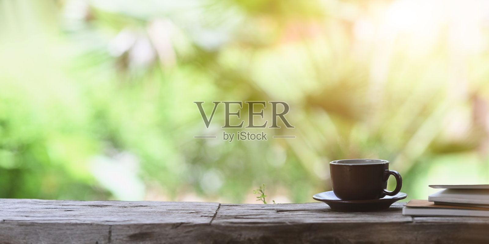 咖啡早晨的概念，咖啡杯和小碟放在旧木板上，和一叠笔记本一起放在森林外面为背景。照片摄影图片