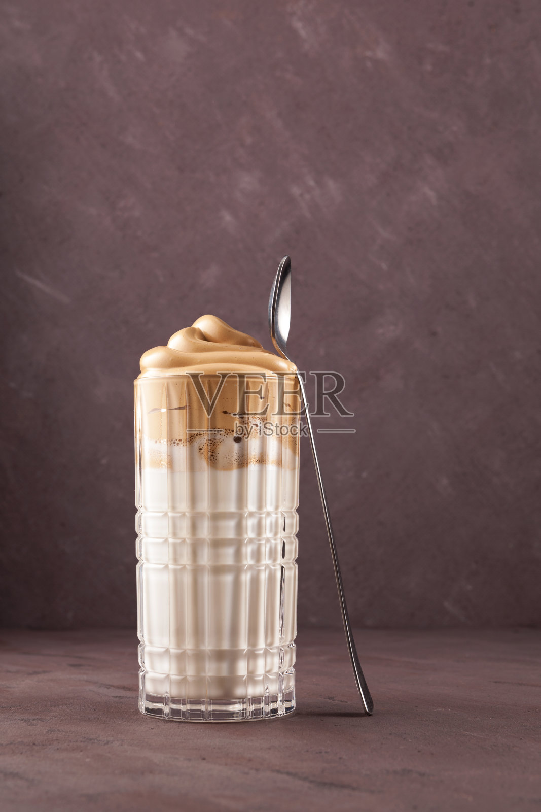 用透明高脚杯自制的达尔戈纳咖啡。受欢迎的韩国饮料拿铁与泡沫速溶咖啡照片摄影图片