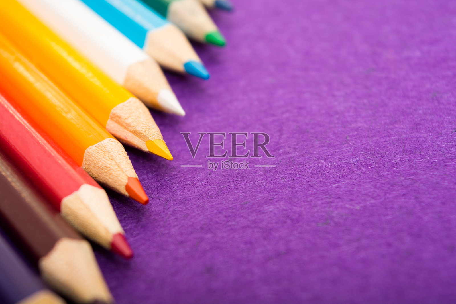 九支彩色铅笔在紫色的毛毡背景上。不同颜色的铅笔与空间的文本。回到学校。照片摄影图片
