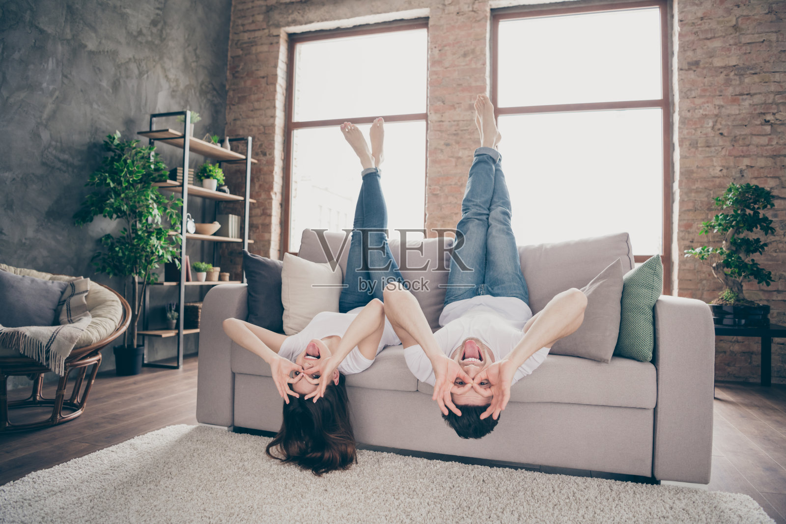 迷人的可爱的，愚蠢的，幼稚的，滑稽的，愉快的，愉快的，疯狂的，顽皮的夫妇躺在沙发上，可以唱歌，像玻璃一样呆在现代工业阁楼风格的砖室内房子照片摄影图片