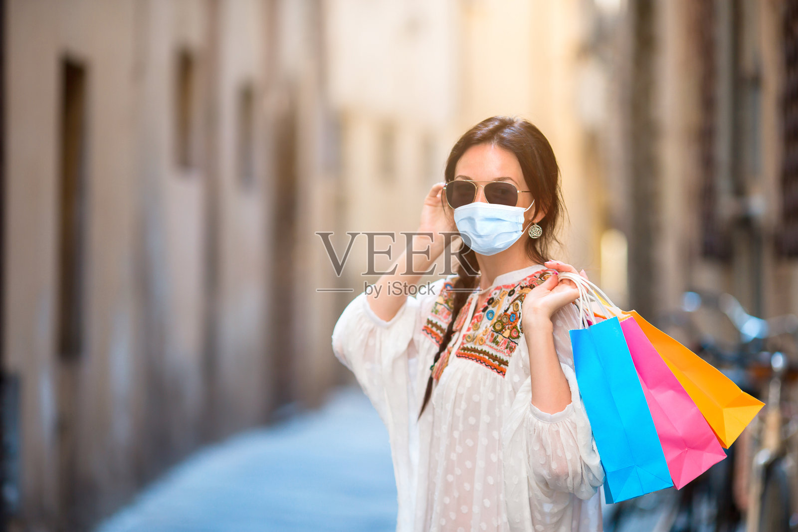 年轻女孩拿着购物袋走在欧洲狭窄的街道上。照片摄影图片