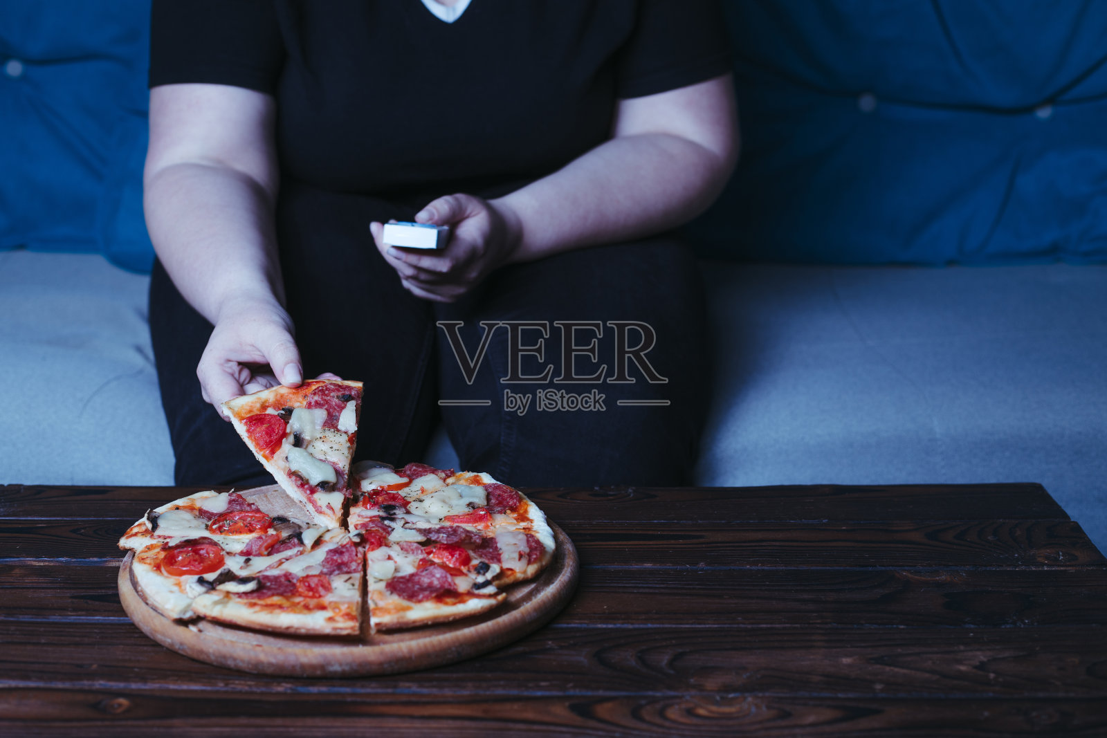 身材偏胖的女人坐在沙发上吃披萨喝啤酒照片摄影图片