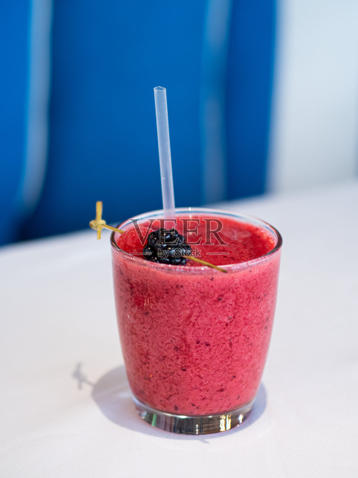 覆盆子黑莓冰沙。素食冷饮加冰。红色和黄色。一个玻璃杯放在一块白桌布上。这种饮料用浆果装饰。餐厅菜单;酒吧和咖啡馆。照片摄影图片