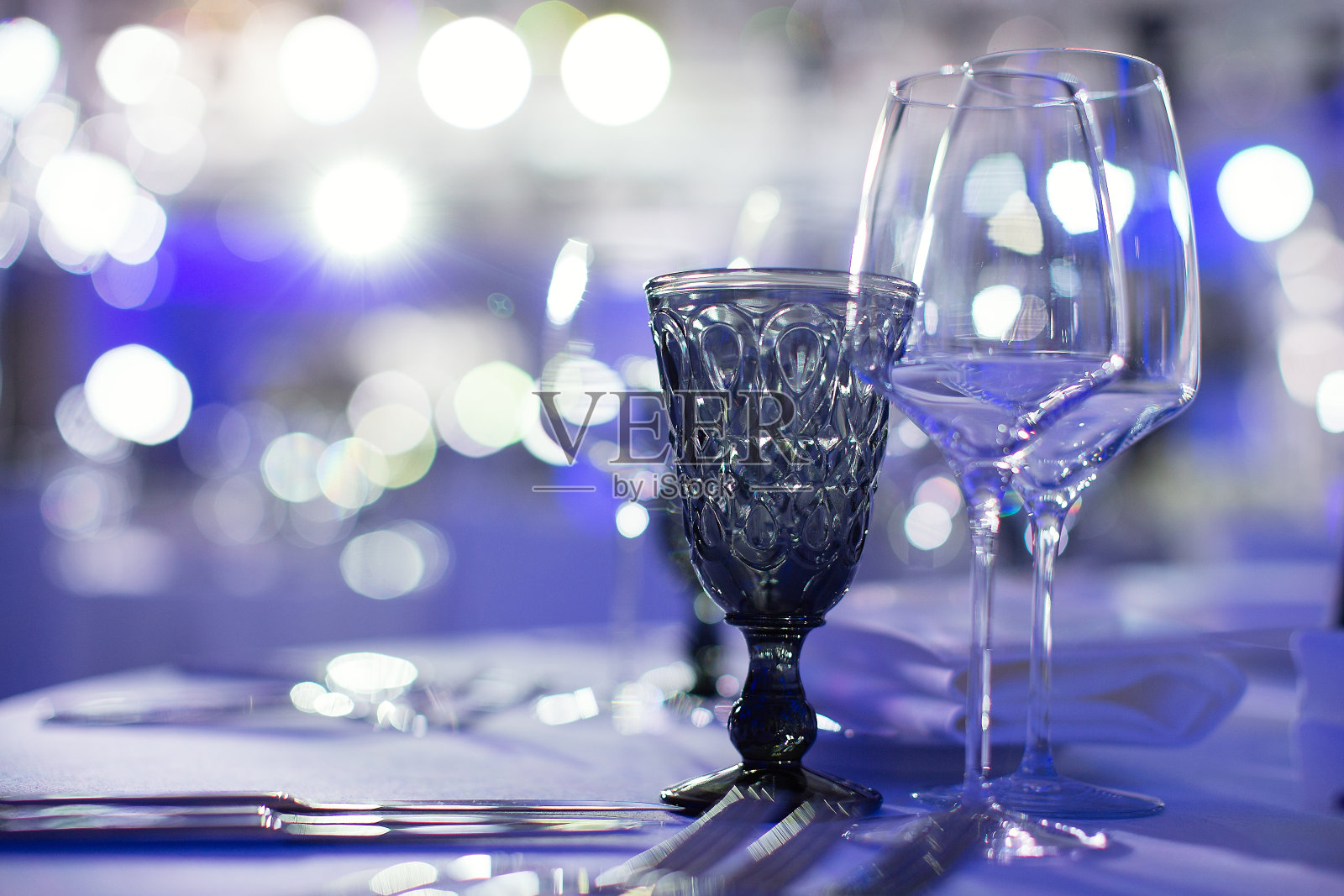 蓝色的背景上放着酒杯，一只漂亮的酒杯在灯光下闪闪发光，耀眼夺目，照片摄影图片
