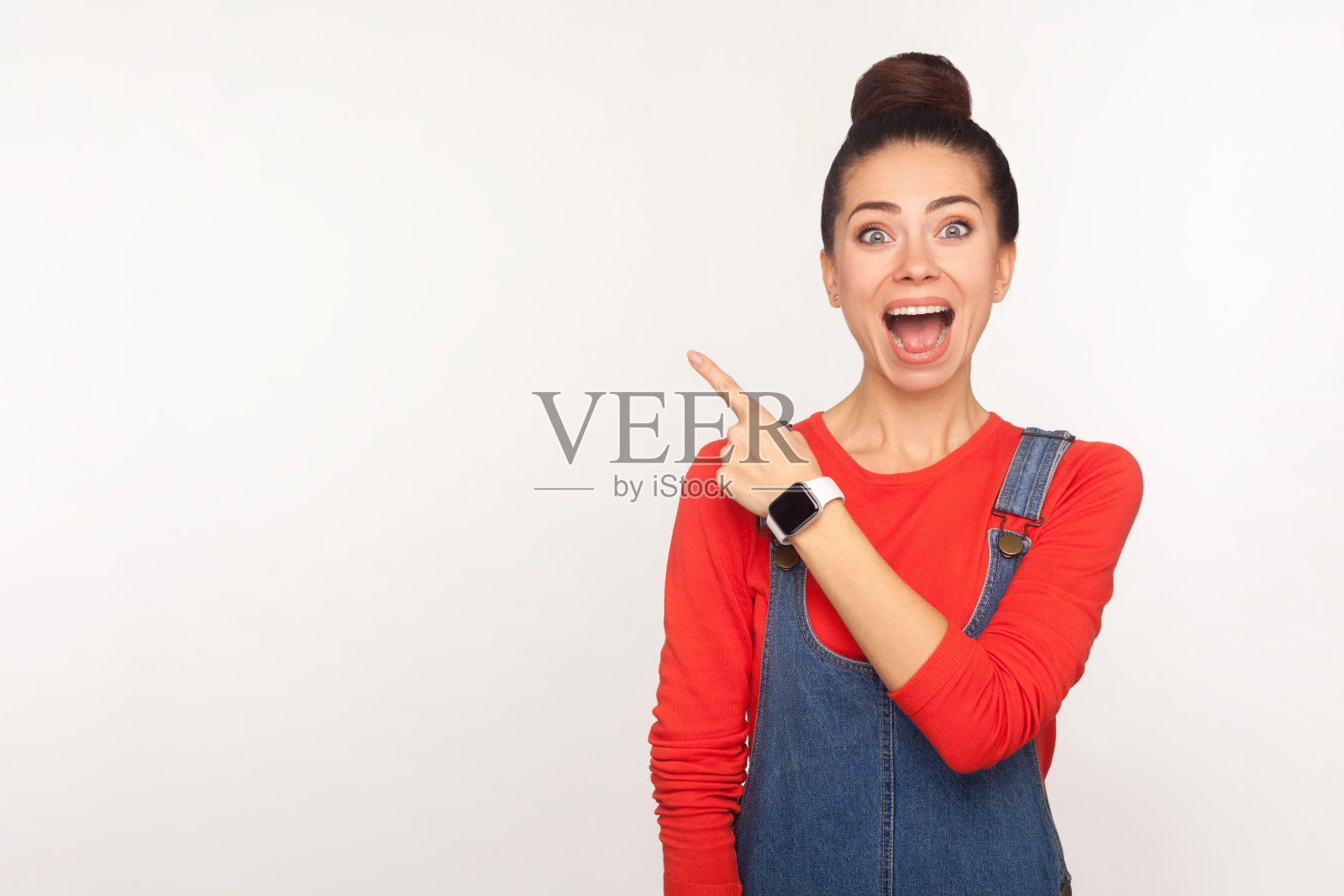 哇，关注广告!肖像惊讶震惊的女孩在牛仔工装裤指着一边复制空间照片摄影图片