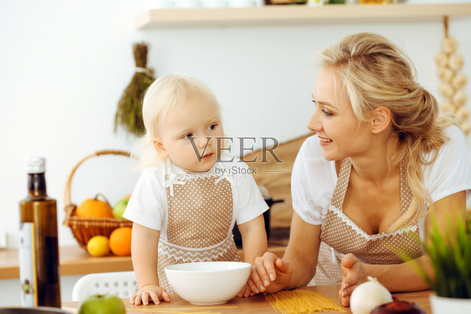 快乐的妈妈和小女儿在厨房做饭。花时间在一起，家庭乐趣的概念照片摄影图片