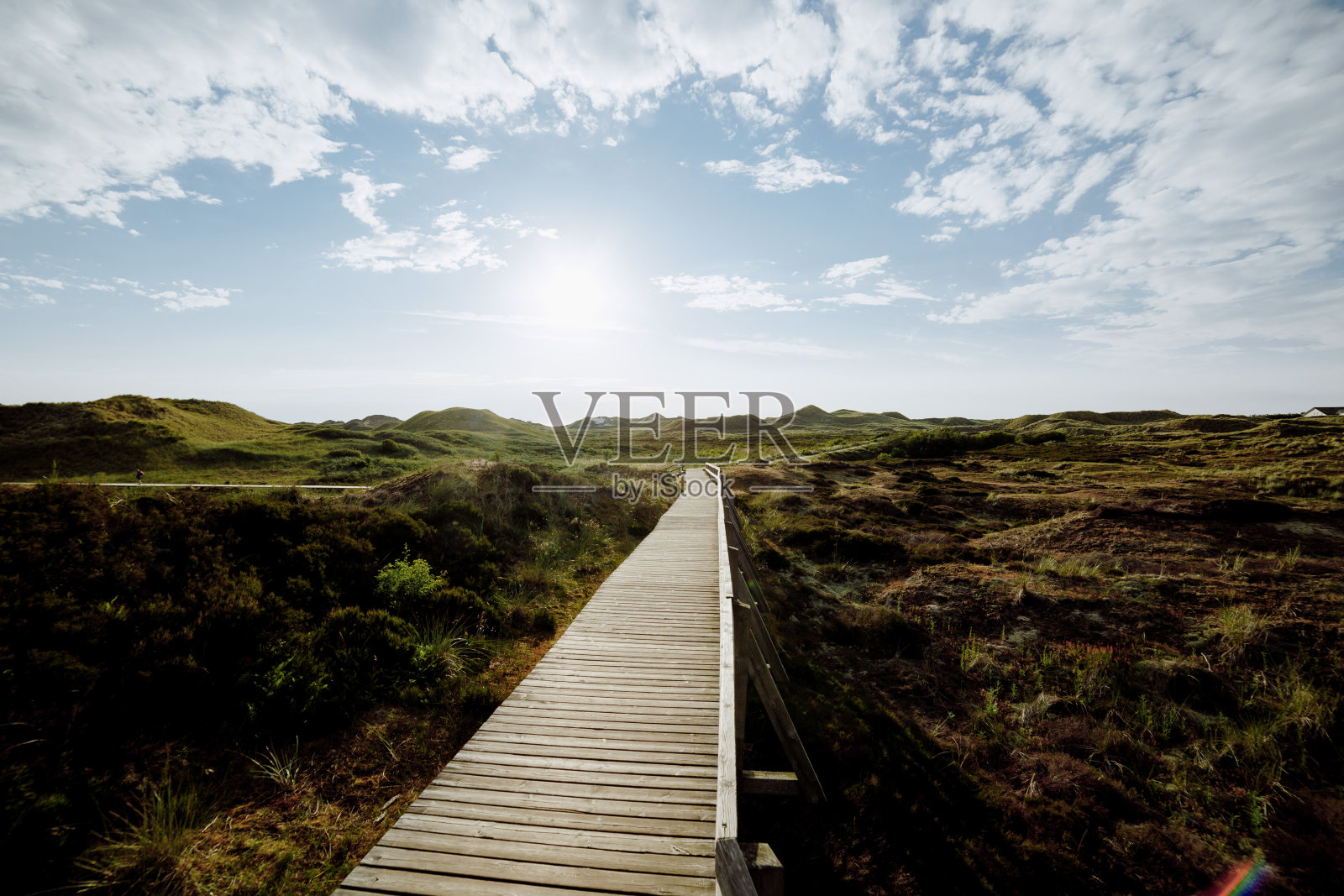 废弃的木板路通过海岸沙丘植被通向一个发光的多云的日落。照片摄影图片
