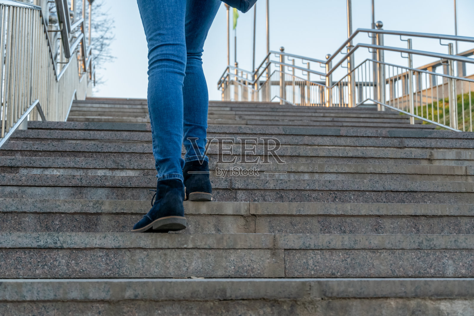一个穿着牛仔裤和蓝色鞋子上楼的女人的腿的特写照片摄影图片