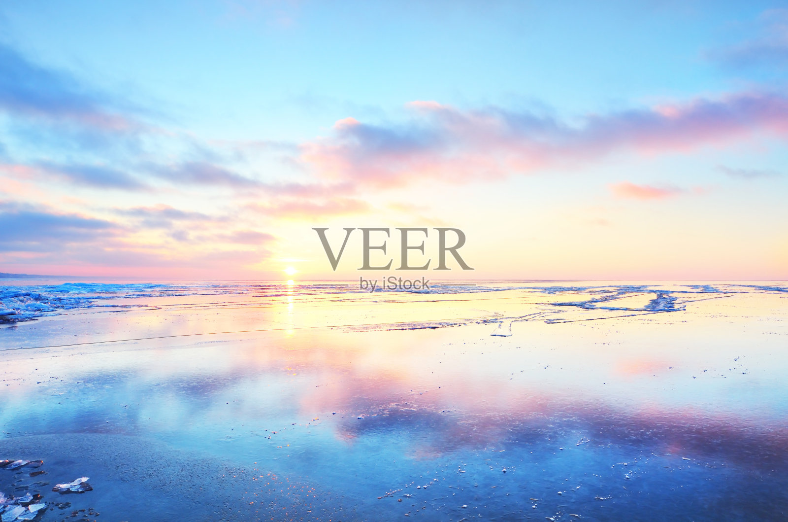 日落时分，冰雪覆盖的萨马湖岸边的全景。冰碎片特写。多彩的cloudscape。水面上对称的倒影。芬兰照片摄影图片