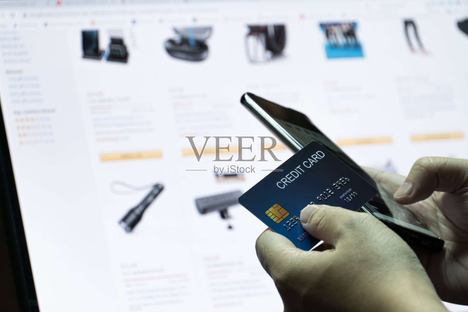 近距离浅层聚焦手持信用卡和手机与电子商务网站在监控背景。照片摄影图片