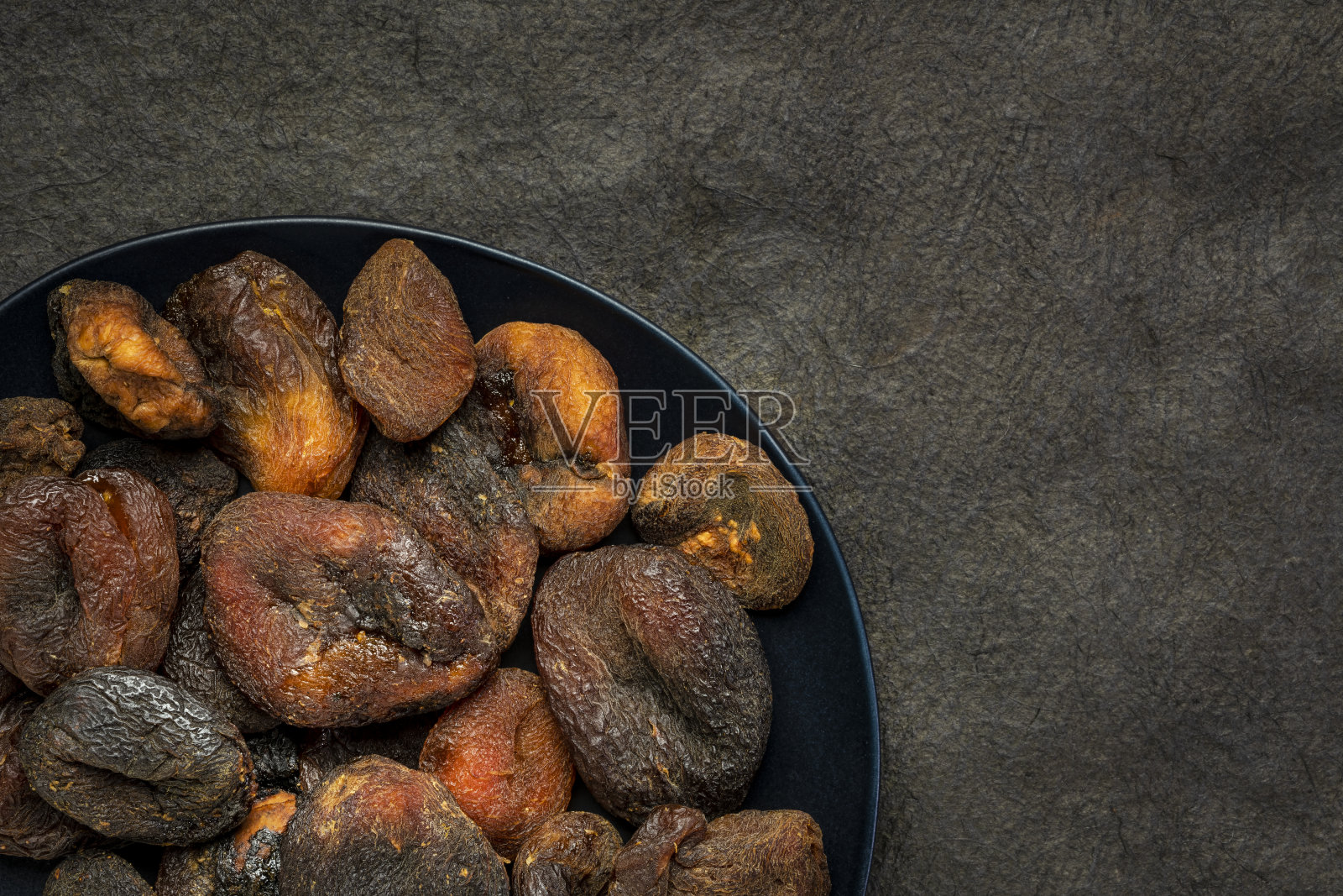 晒干的杏子放在黑盘子里照片摄影图片