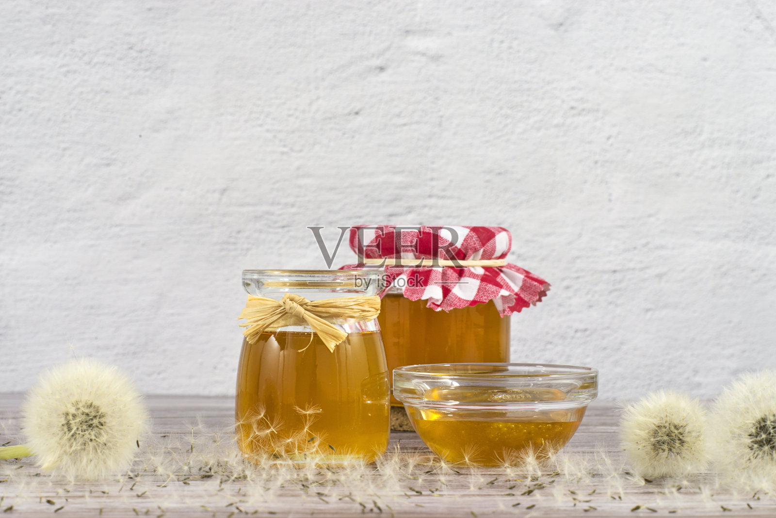蒲公英果酱、蜂蜜、果冻在一个玻璃罐里放在木桌上，白色的背景上有鲜花，蒲公英轻快的种子头、种子、吹球。药物、健康食品、健康受益于自然照片摄影图片