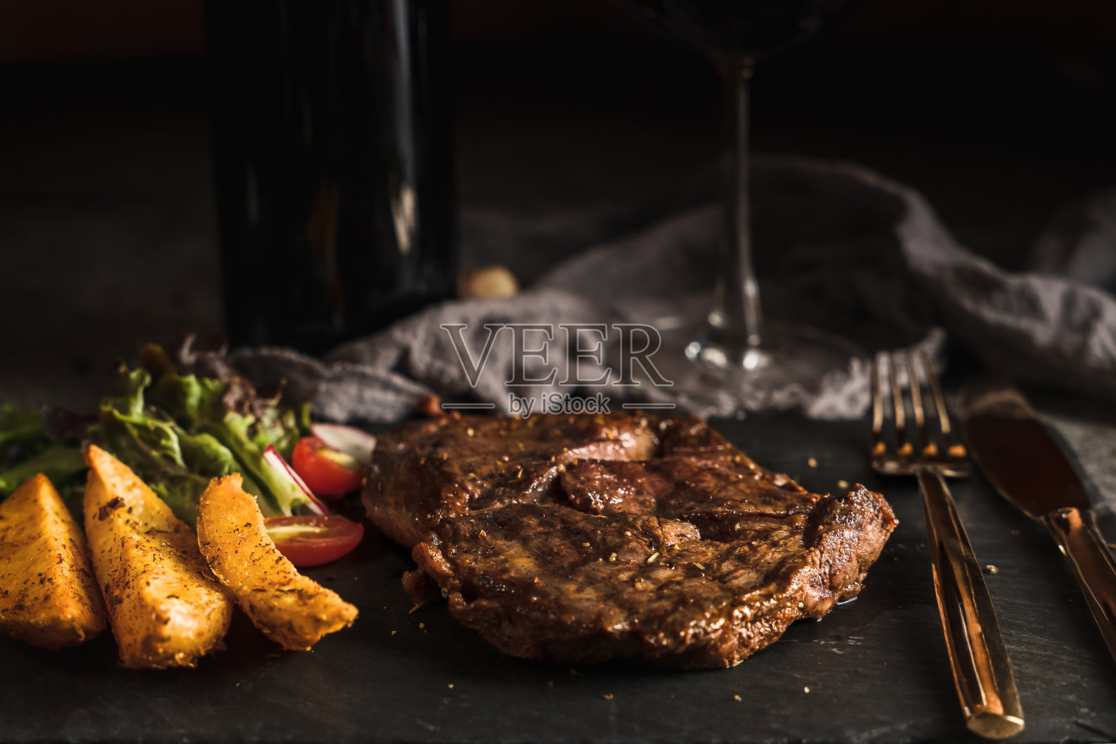 食物背景:牛肋眼牛排，黑胡椒酱，烤土豆，蔬菜沙拉，黑石板石，红酒，有选择的重点照片摄影图片