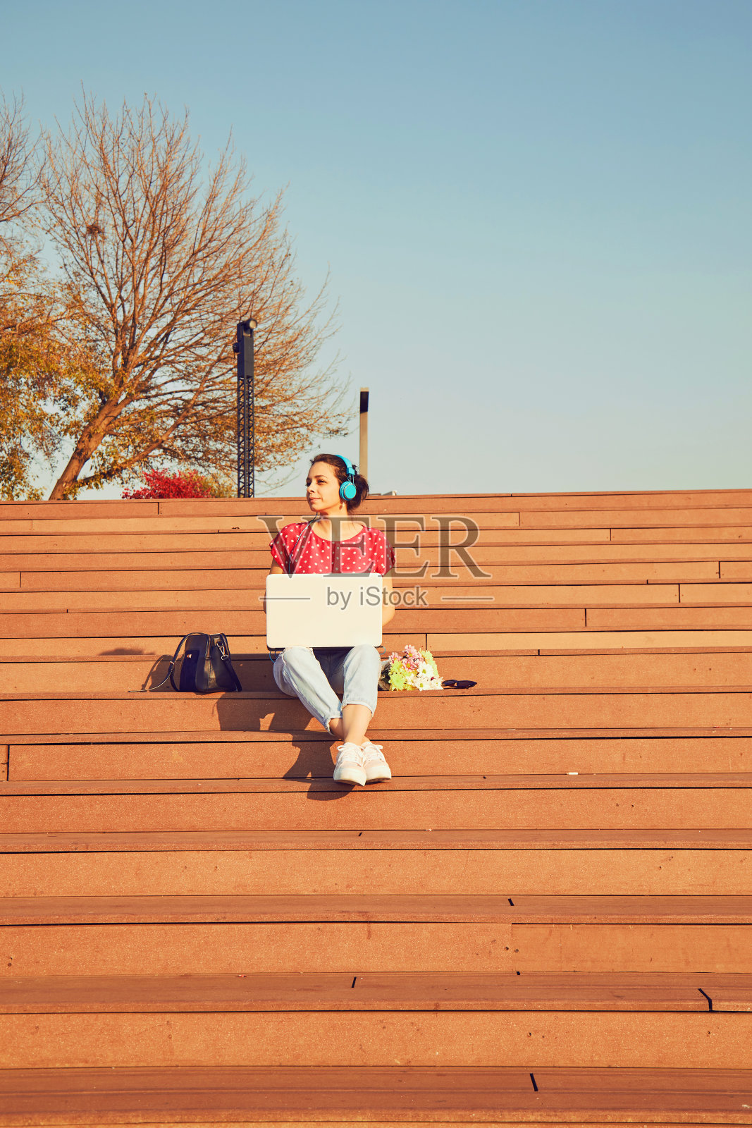 在笔记本电脑上工作，在户外听音乐的漂亮女人。照片摄影图片