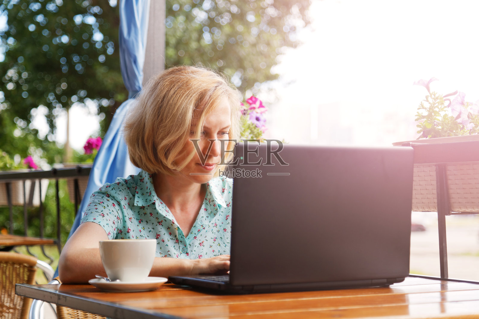 一个女人正坐在桌子旁，手里拿着一台笔记本电脑和一杯咖啡照片摄影图片