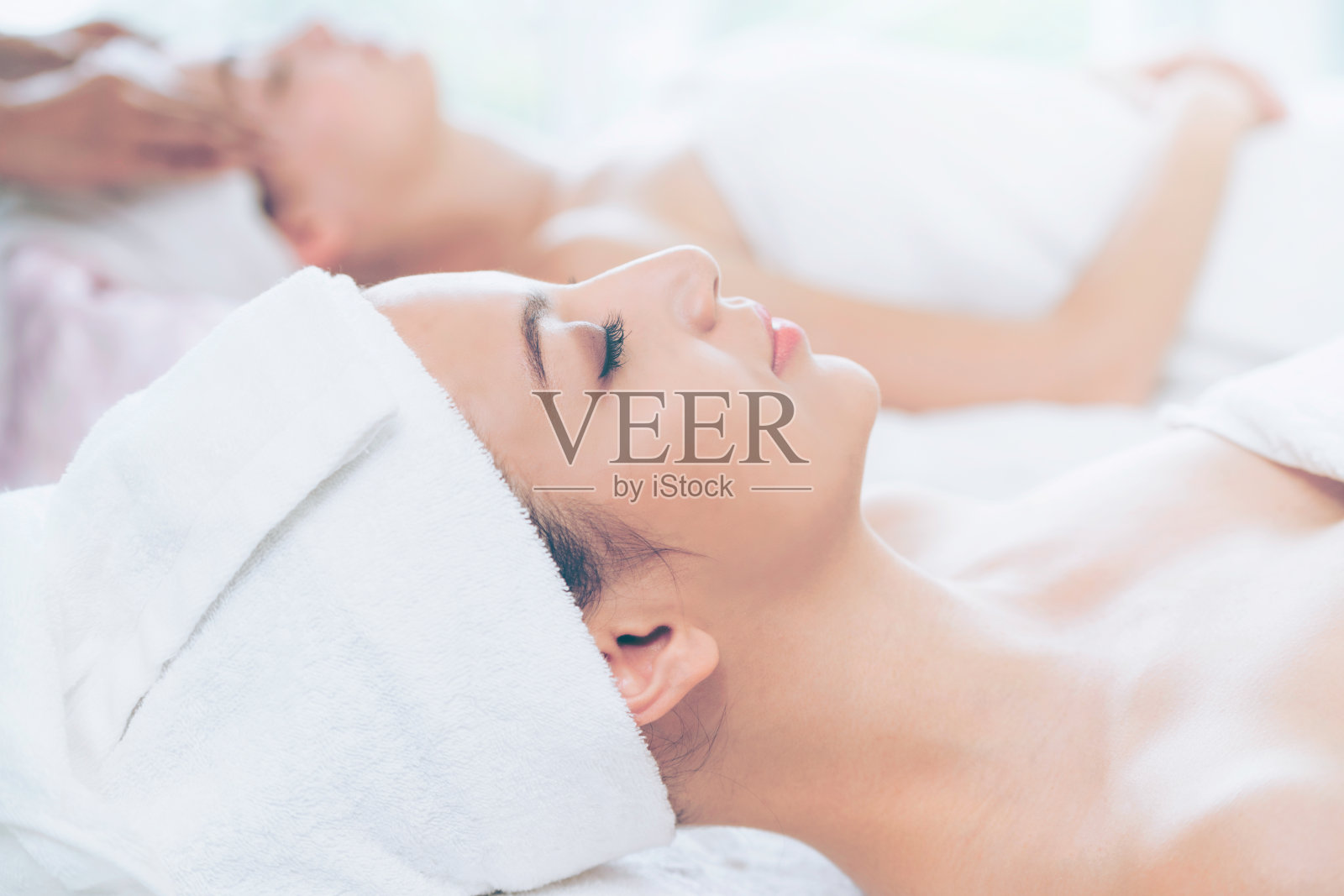 放松的年轻女子躺在水疗床上按摩。照片摄影图片