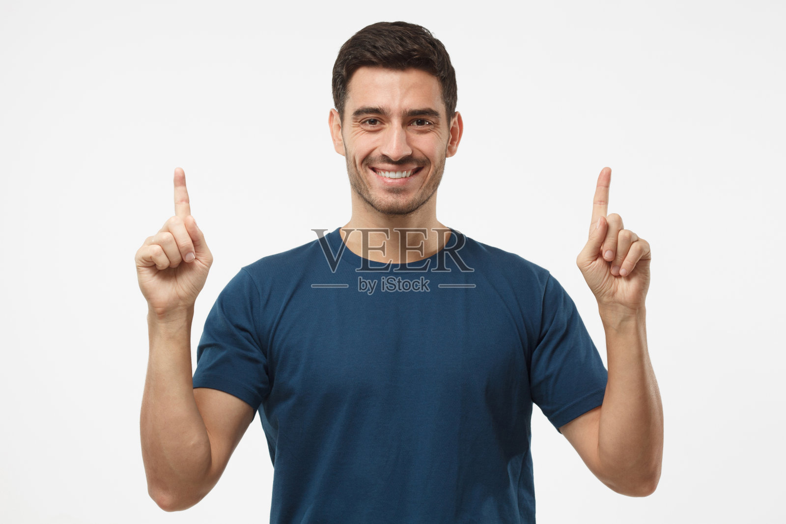 穿着蓝色t恤的英俊男子，两根手指分别指向灰色背景照片摄影图片