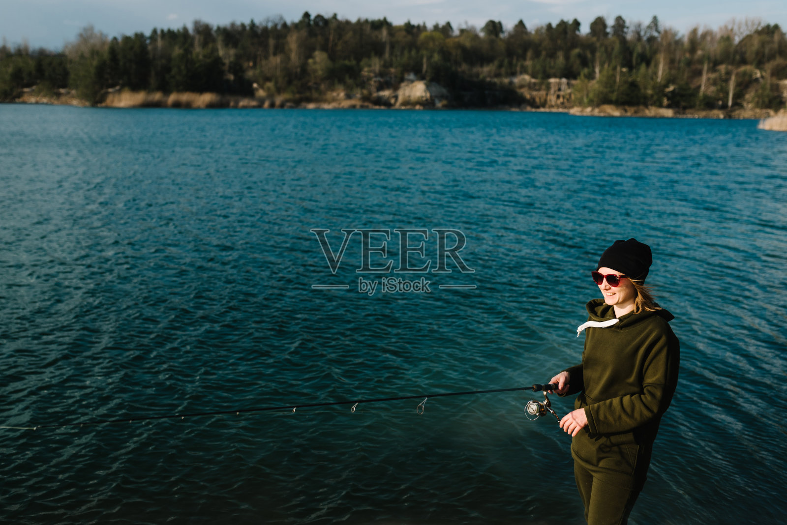 周末在湖或池塘钓鱼时，妇女用拉杆钓鱼。渔夫拿着钓竿，在河岸上旋转卷轴。日出。捕狗鱼、鲈鱼、鲤鱼。大自然的背景。照片摄影图片
