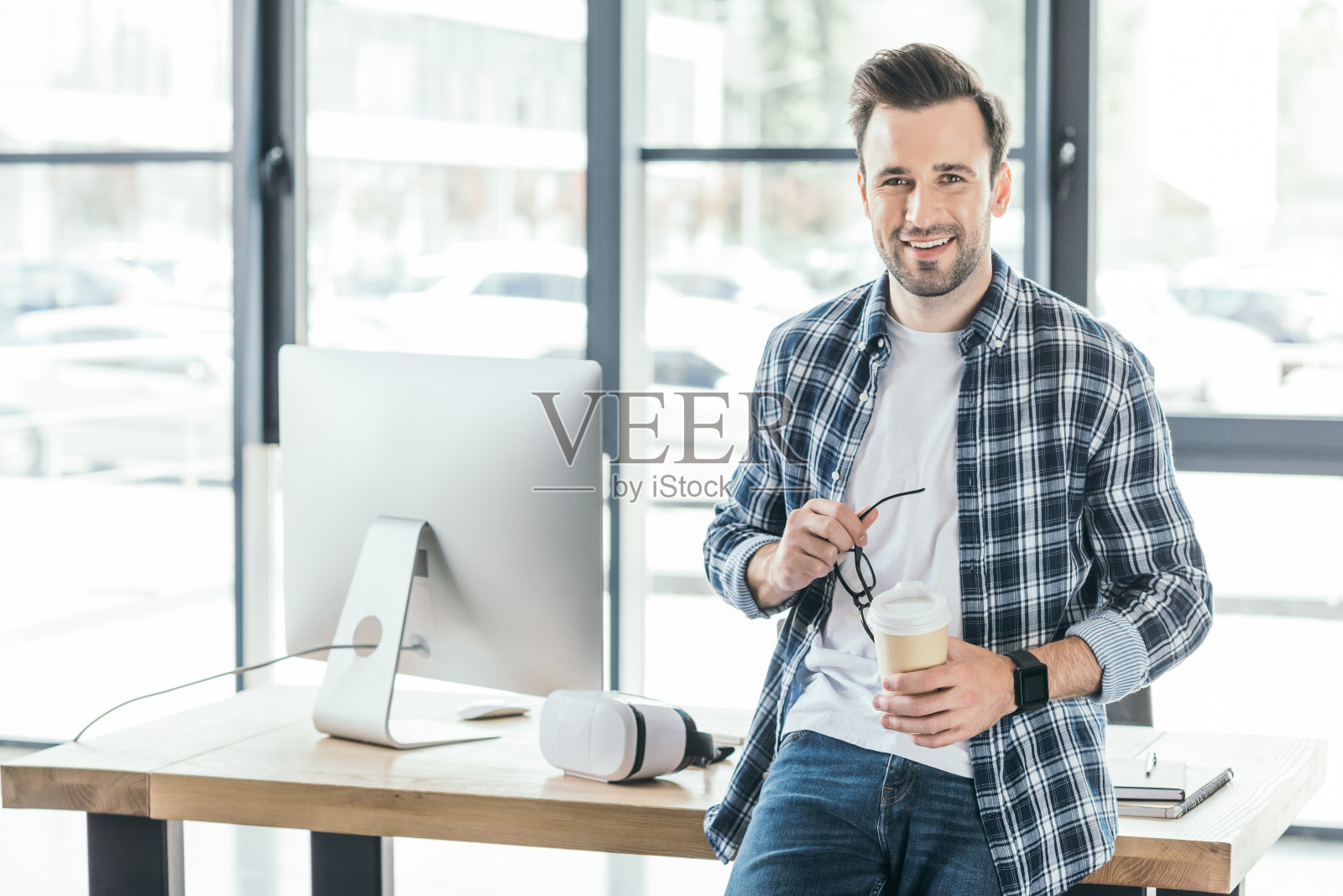 一名年轻人在工作场所拿着眼镜和纸杯对着镜头微笑照片摄影图片