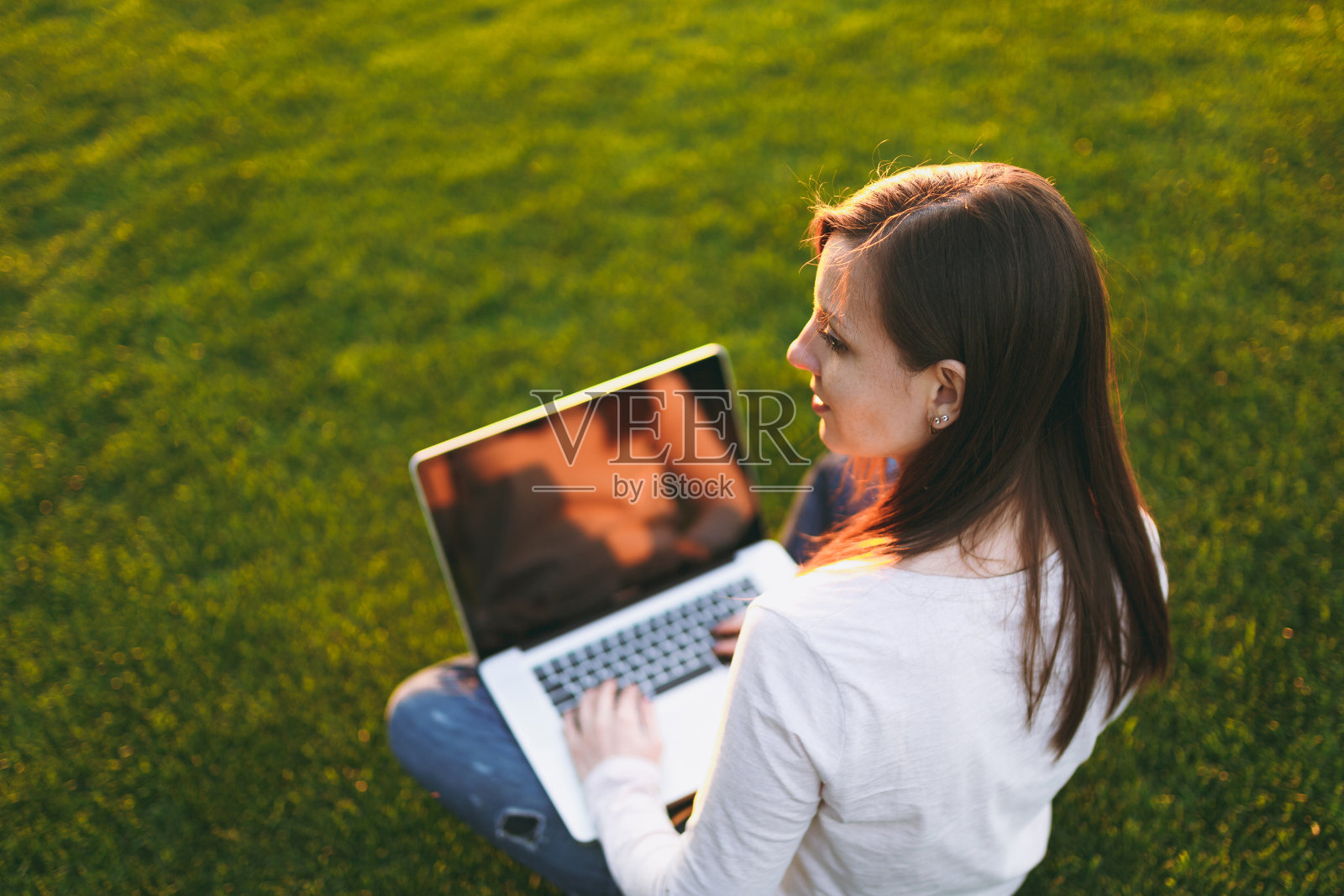 年轻女性的后视图。女人工作的笔记本电脑与空白的黑色空白屏幕拷贝空间在城市公园在绿色的草地阳光草坪户外。移动办公室。自由经营理念。照片摄影图片