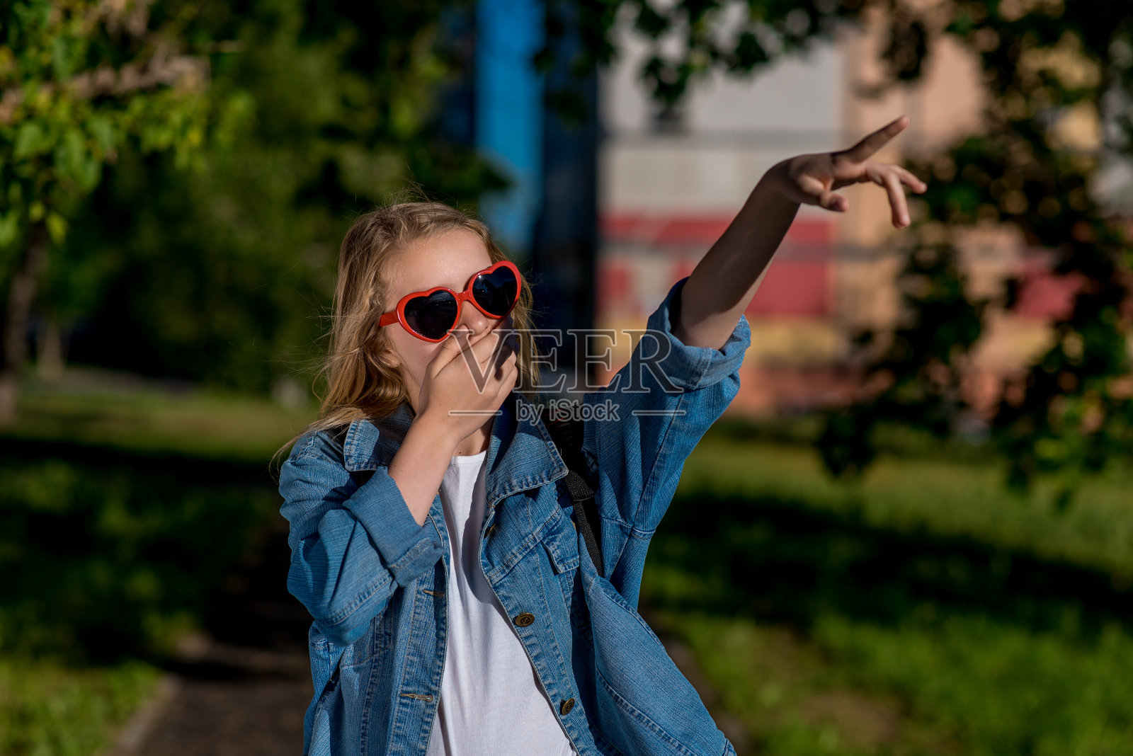 女孩女生。夏天在自然。心形的太阳镜。手指他的手指向一边。惊喜的概念是惊喜。喜悦的情绪，愤怒的情绪。照片摄影图片