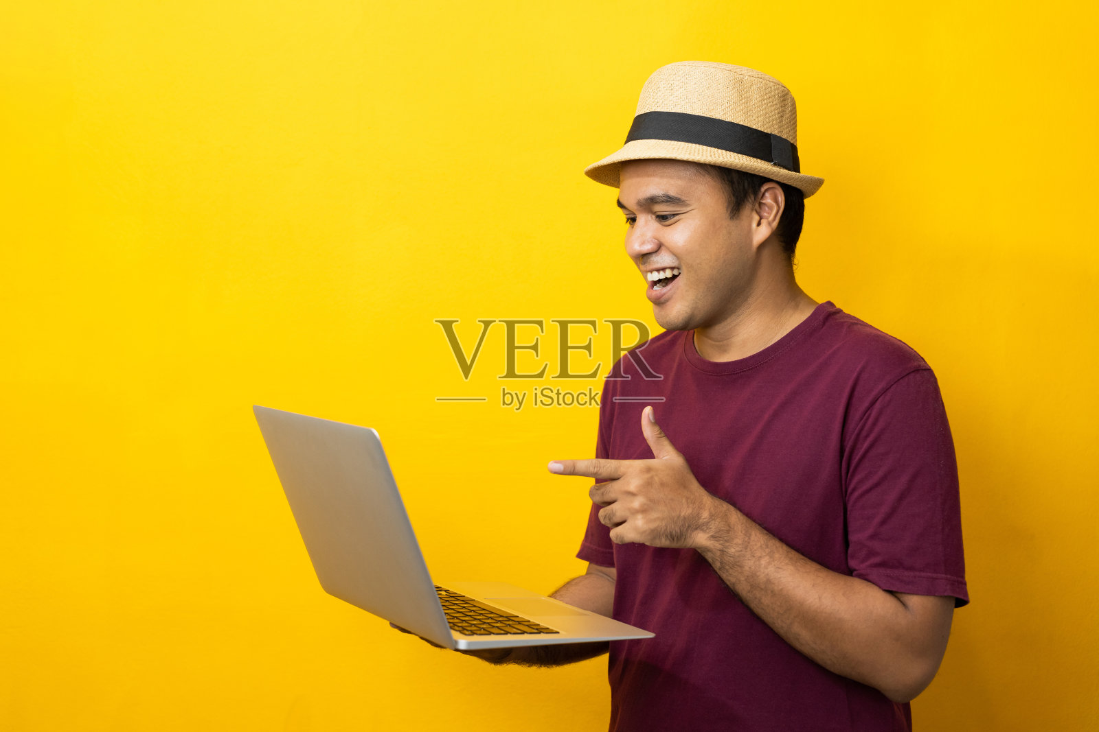 亚洲人红色衬衫与帽子使用笔记本电脑在孤立的黄色背景。照片摄影图片