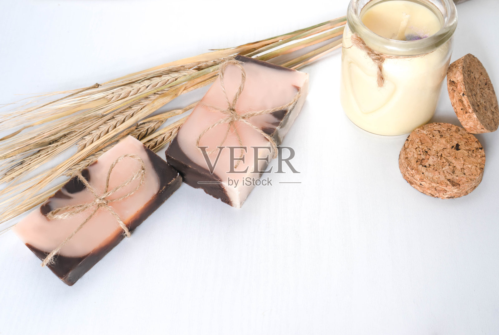 由两个手工制作的带有橙色色调的棕粉色肥皂，柔和的香草蜡烛和小麦穗组成的白色背景和木质纹理。水平的照片。手工化妆品概念与天然成分的个人护理，洗澡照片摄影图片