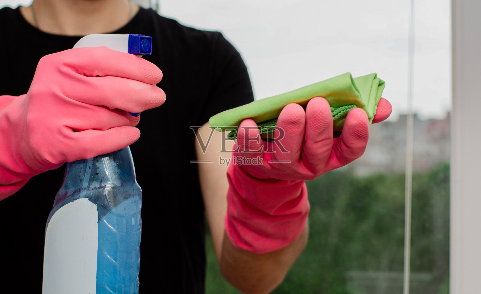 一个戴着粉色橡胶手套的年轻人拿着窗户清洁剂和抹布，在清洗塑料窗户照片摄影图片