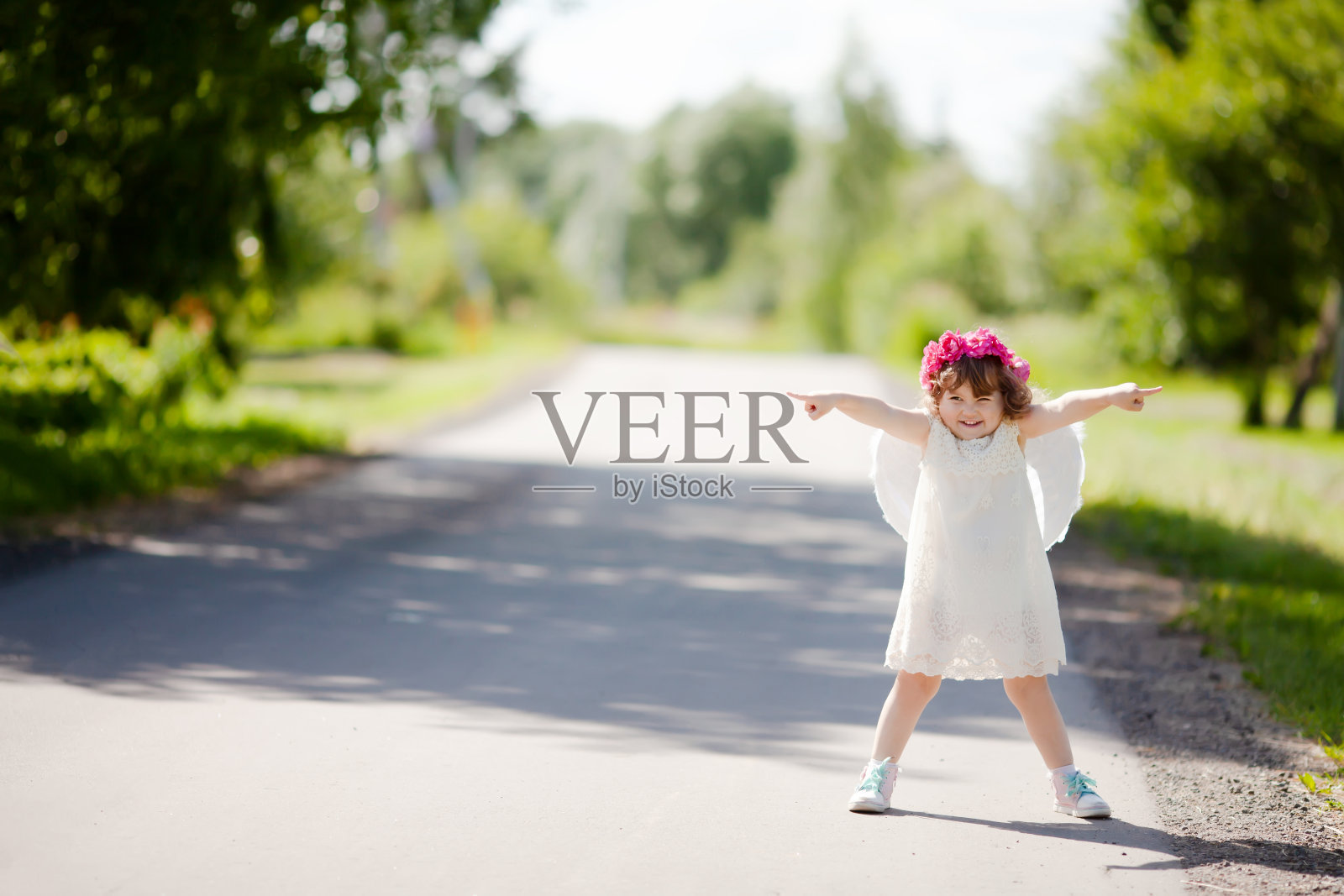 可爱的小天使戴着花圈，站在路边，微笑着逗弄人照片摄影图片