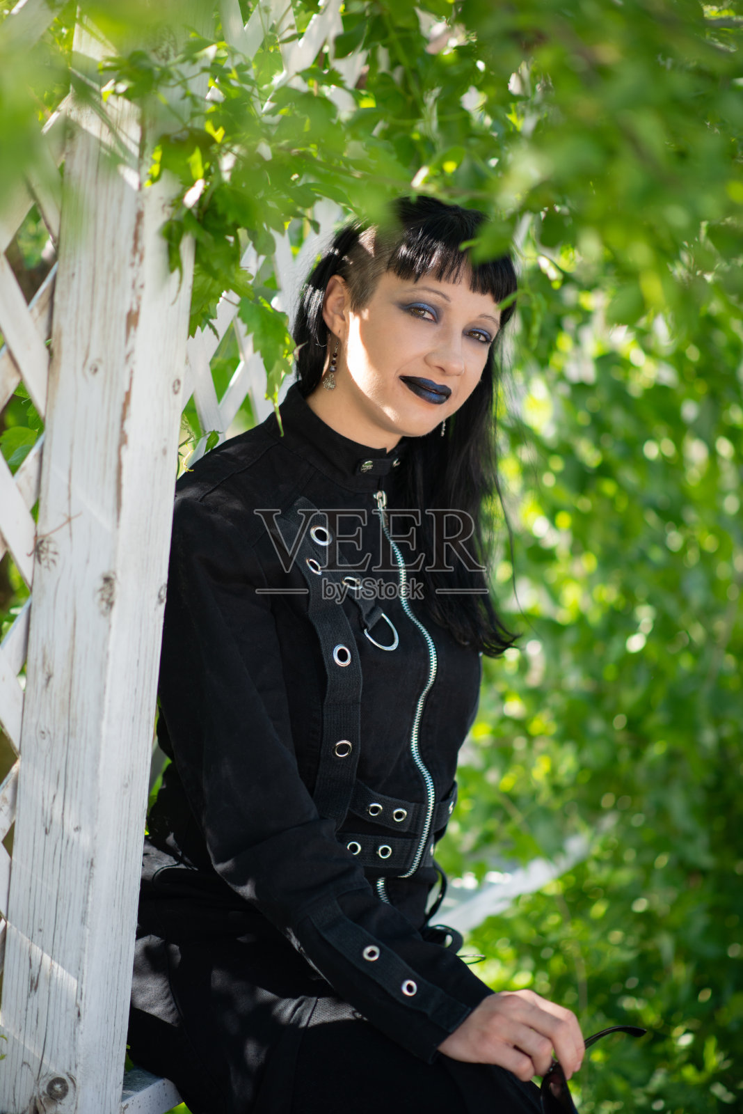 穿着哥特式服装，坐在格子篱笆旁的女人，穿着斑驳的阴影。照片摄影图片