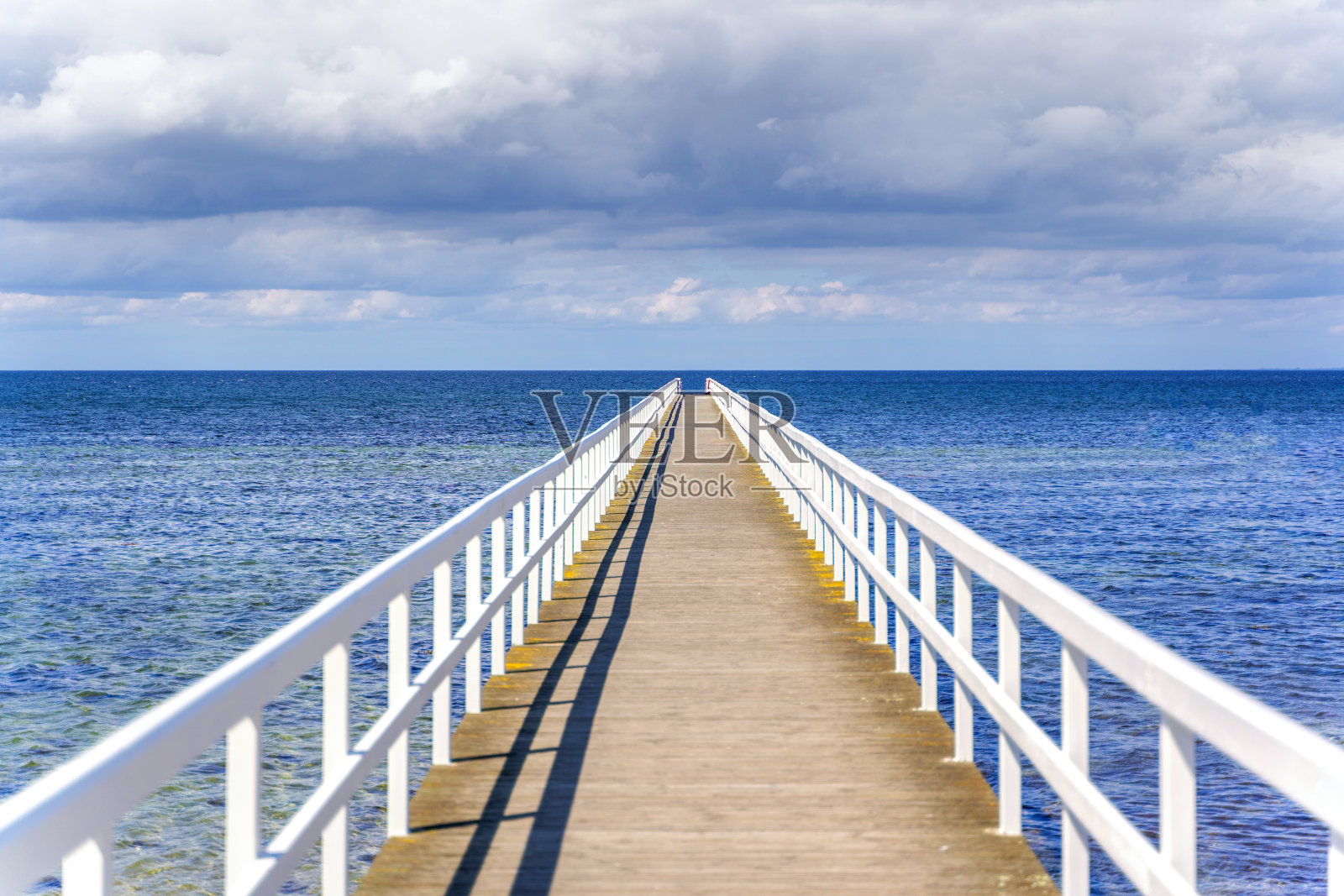 木制的白色桥通往大海，在长长的码头上可以看到壮观的天空。照片摄影图片