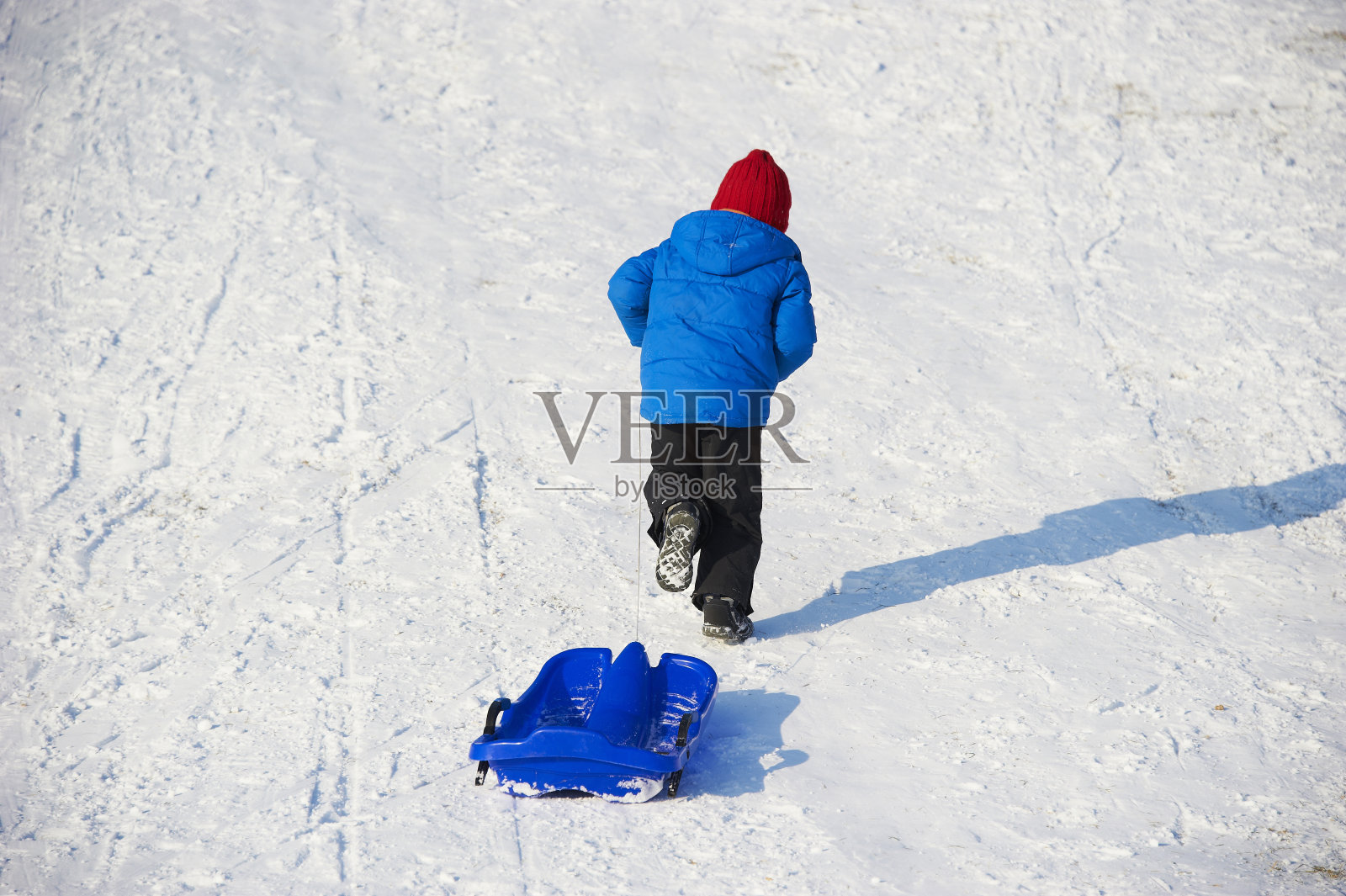 带着雪橇的小男孩在城市公园里散步。照片摄影图片