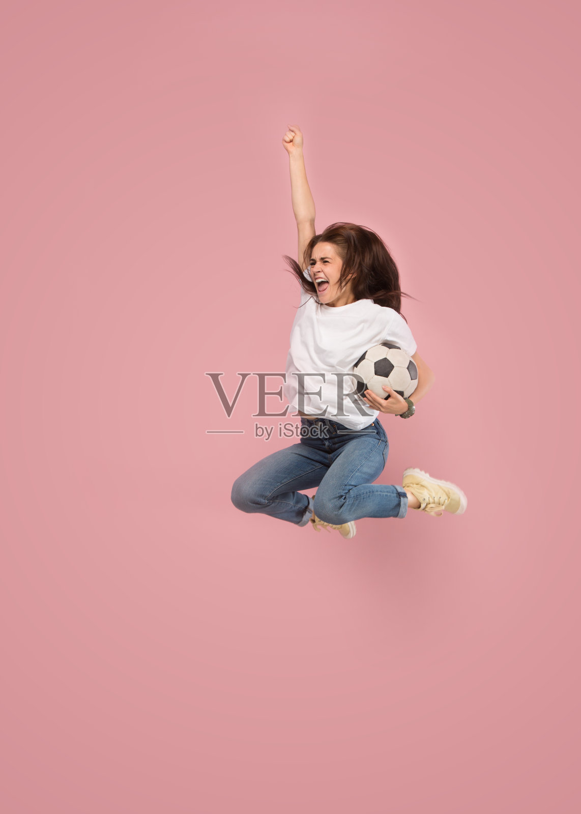 向胜利前进。那个年轻的女人就像足球运动员一样，在录音室里跳着踢着粉红色的球照片摄影图片
