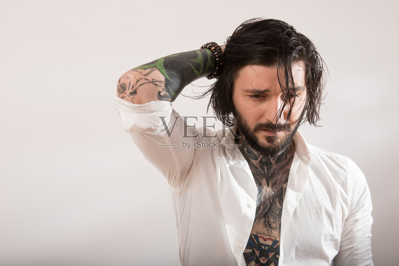 有纹身的男人，凌乱的头发，白色的衬衫向下看照片摄影图片