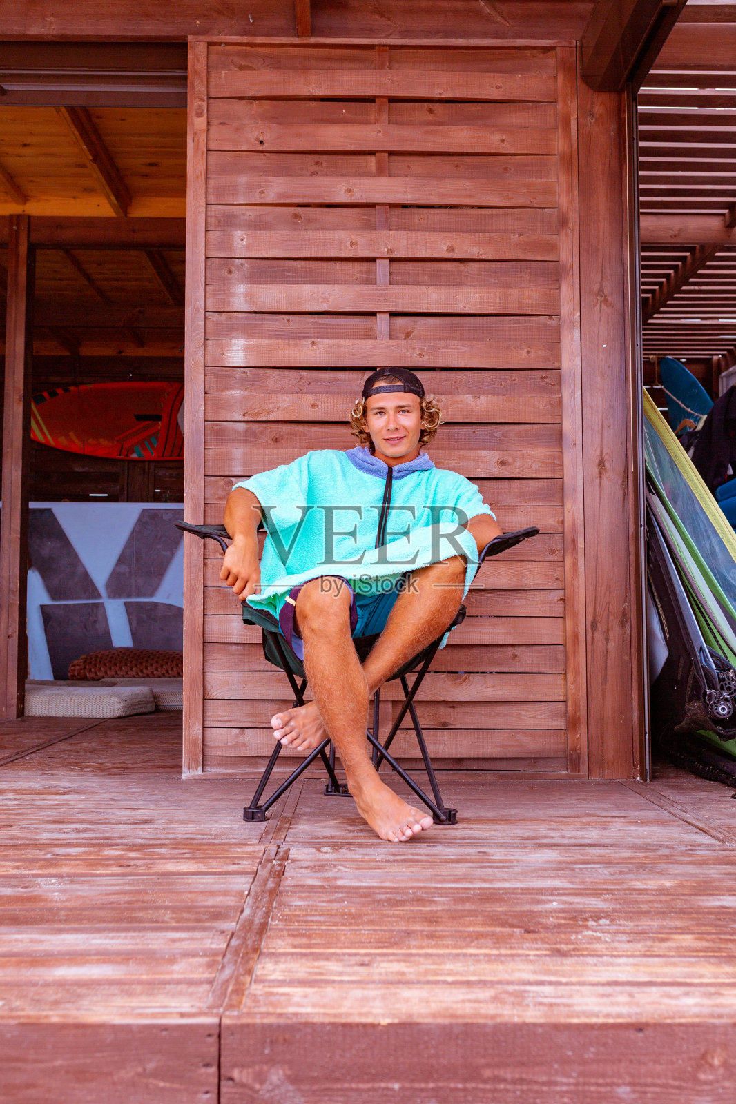 年轻帅气的冲浪者穿着浴袍坐在海边的露台上，放松和看着远处的大海照片摄影图片