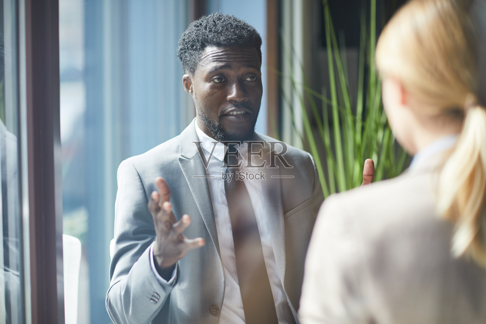 在咖啡馆里，帅气的非洲商人穿着西装，皱着眉头，打着手势与同事分享商业想法照片摄影图片