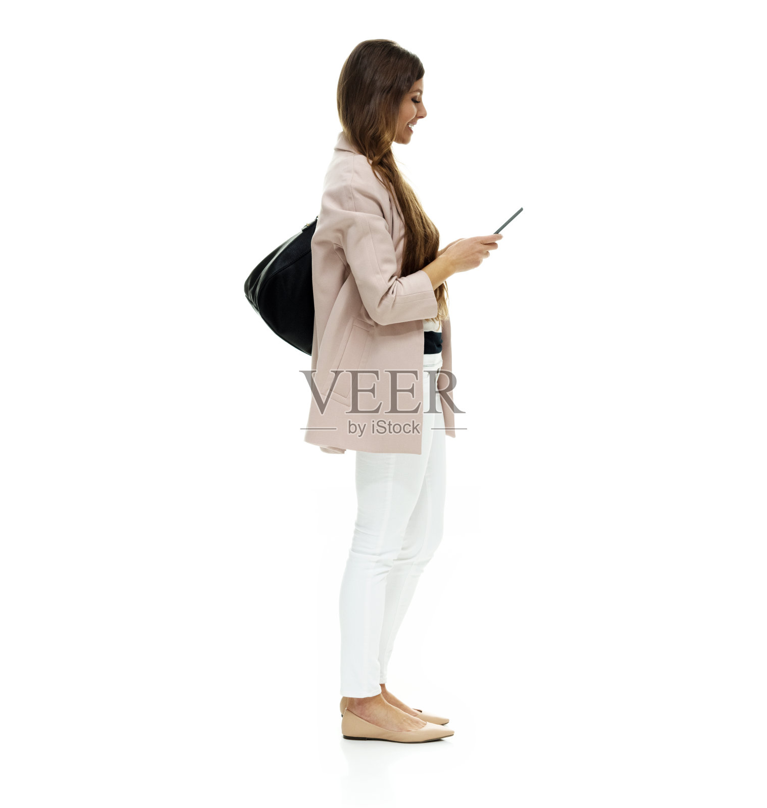 白人女性站在白色背景前，穿着外套，拿着钱包和使用智能手机照片摄影图片