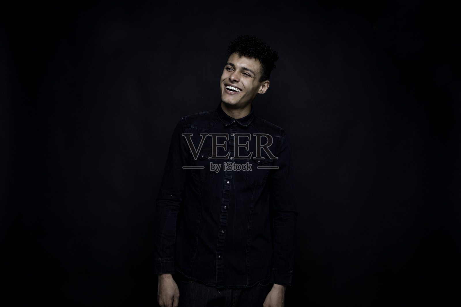 非裔美国人年轻的潮男穿着牛仔裤站在黑色背景前照片摄影图片