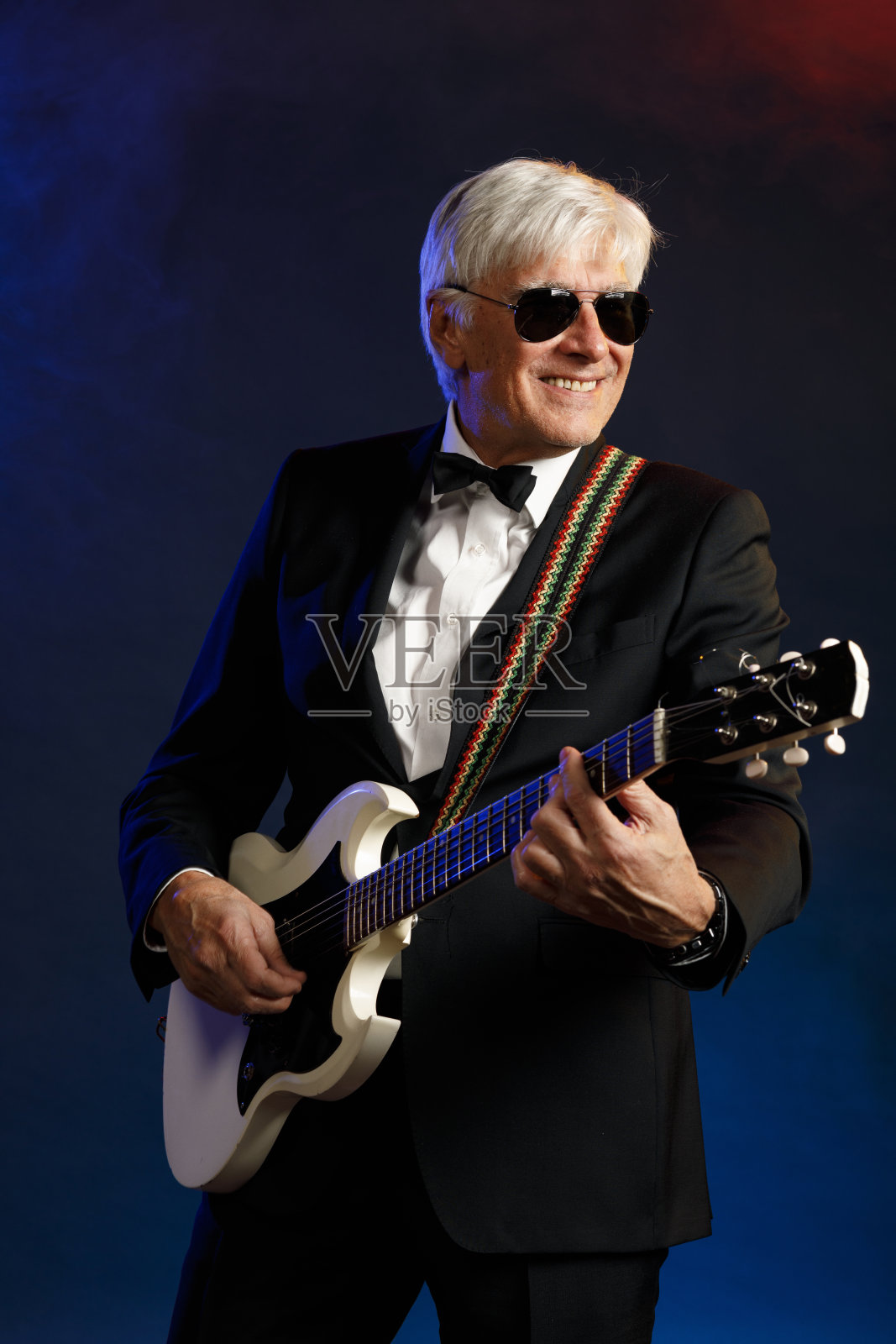 音乐家吉他手活跃的高级英俊男子弹吉他。蓝色背景，光线和烟雾特效。照片摄影图片