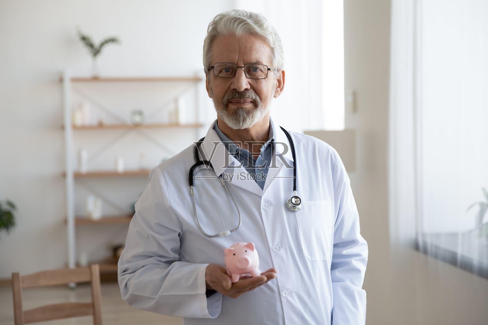 老男医生拿着储蓄罐看着摄像机照片摄影图片