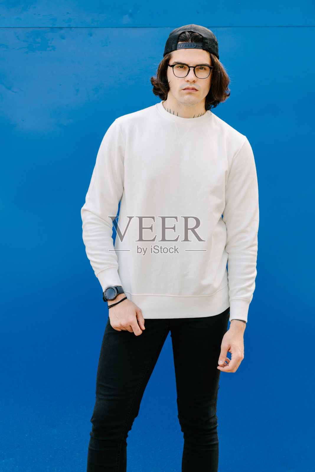 身穿白色运动衫或帽衫，戴眼镜的男子，外面是蓝色背景。运动衫或帽衫的模拟，标志设计或设计印花与自由的空间照片摄影图片