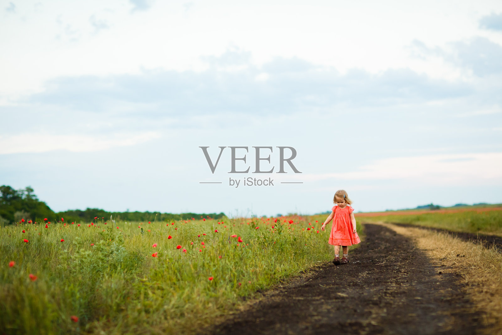 小女孩雨后走在肮脏的土路上。照片摄影图片