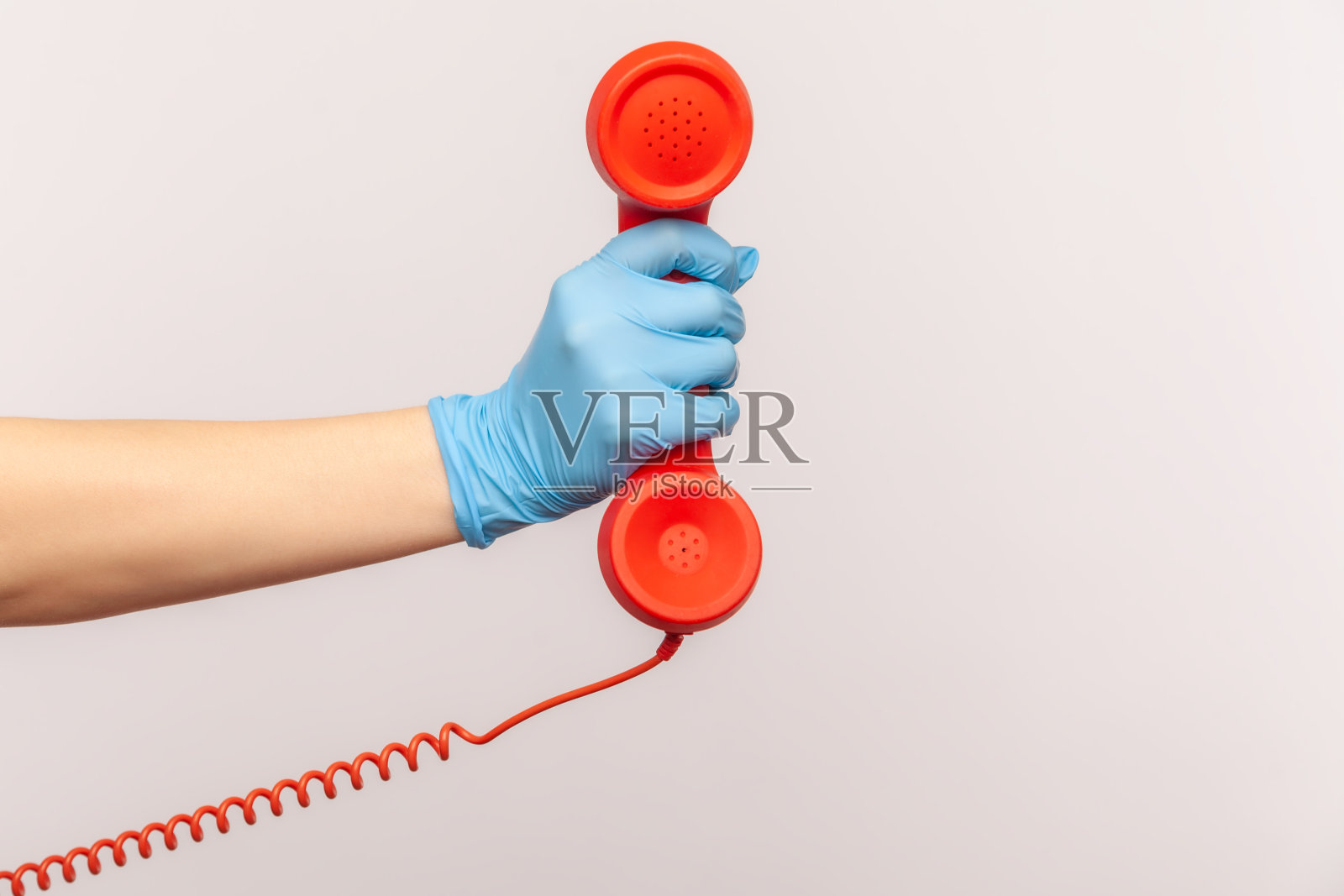 侧面特写的人的手在蓝色外科手套持有和显示红色cale电话听筒。照片摄影图片